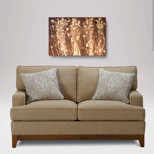 May include: A beige sofa with two pillows featuring a paisley pattern. The sofa is in front of a white wall with a brown abstract painting above it.