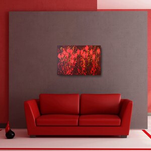 May include: Abstract painting with red, yellow, and black paint splatters on a dark background. The painting is framed and hanging on a gray wall above a red couch.