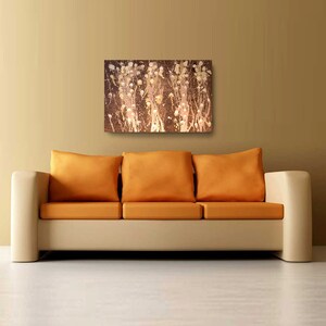 May include: A beige sofa with three orange cushions in front of a brown wall with an abstract painting of white and gold splatter paint on a brown background.