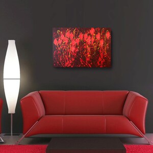May include: Abstract painting with red and yellow paint splatters on a black background. The painting is hanging on a wall above a red couch.