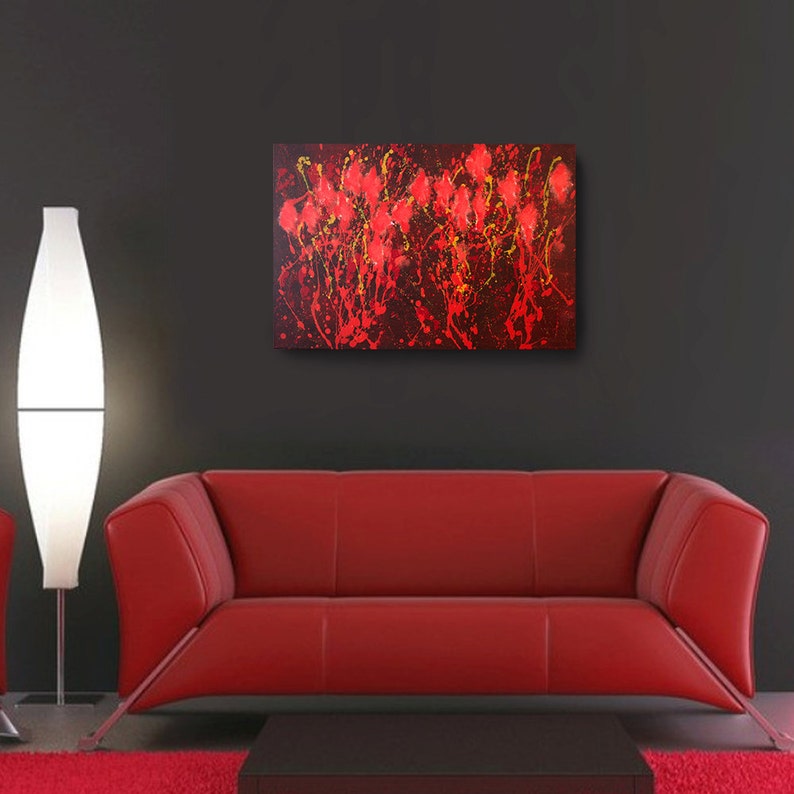 May include: Abstract painting with red and yellow paint splatters on a black background. The painting is hanging on a wall above a red couch.