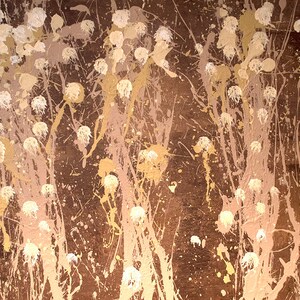 May include: Abstract painting with a brown background and white and gold splatters of paint. The splatters are arranged in a pattern that resembles flowers or trees.