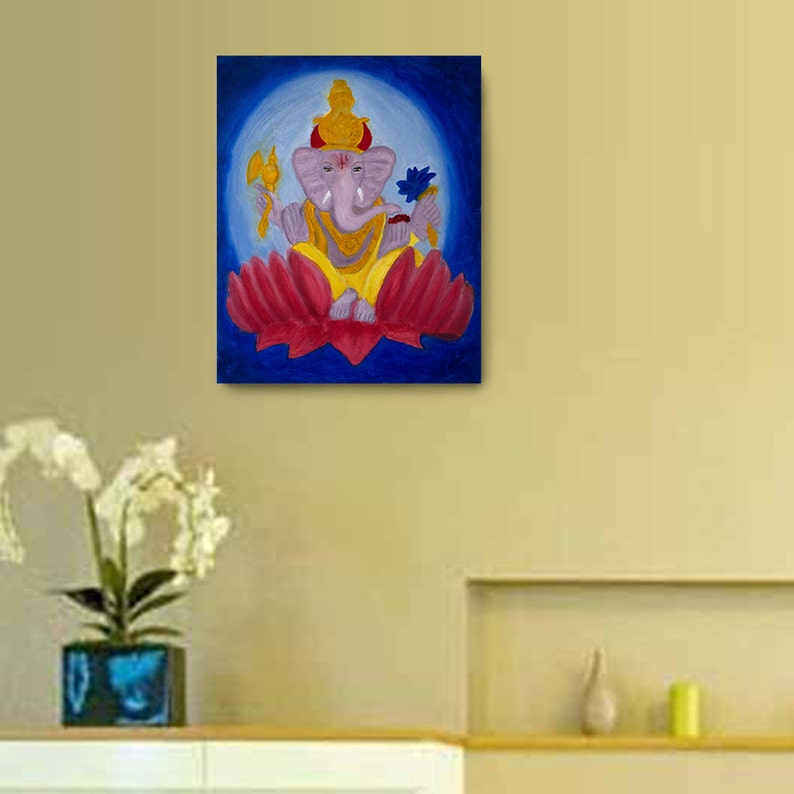 Puede incluir: Pintura de la deidad hind&uacute; Ganesha, representada con cabeza de elefante, sentada sobre una flor de loto roja. Sostiene una flor azul en una mano y un hacha en la otra. El fondo es azul con un halo blanco alrededor de Ganesha.