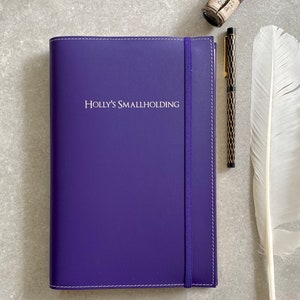 Könnte beinhalten: Ein violettes, ledergebundenes Tagebuch mit dem in weiß geprägten Text "HOLLY'S SMALLHOLDING" auf dem Einband.
