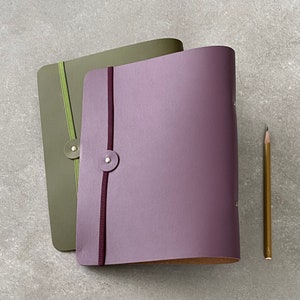 May include: Two leather-bound notebooks with elastic closures. The top notebook is green and the bottom notebook is purple.