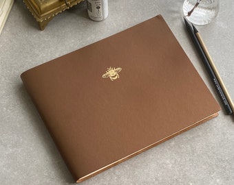 Elevate your guest book experience with our Recycled Leather Guest Book featuring a stunning gold bee icon, in a spectrum of 26 colours.