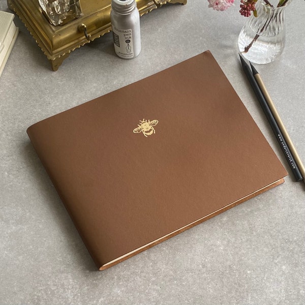 Elevate your guest book experience with our Recycled Leather Guest Book featuring a stunning gold bee icon, in a spectrum of 26 colours.