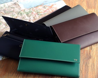 May include: Five leather wallets in different colors, including green, brown, gray, and black. The wallets are closed and arranged in a stack. The top wallet is green and has the initials "TM" embossed on the front.