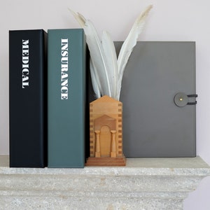 May include: Three gray leather binders with the words "MEDICAL" and "INSURANCE" printed in white on the front. The binders are on a stone shelf with a wooden decorative piece in the center.