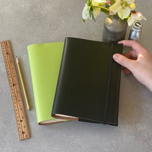 May include: Two leather-bound journals, one green and one black, with a brown elastic closure on the black journal.