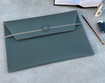 Op de afbeelding: Een donkergrijze leren envelop met een grijs elastiek en een zilveren knoopsluiting.