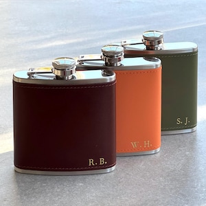 May include: Three leather-covered hip flasks in burgundy, orange, and olive green. Each has a silver cap and trim. The burgundy flask is engraved with "R. B.", the orange with "W. H.", and the green with "S. J."