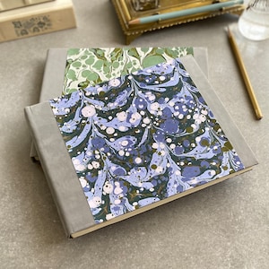 May include: A gray hardcover journal with a blue and green marbled paper cover. The journal is closed and lying on a gray surface.