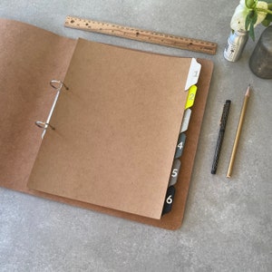 May include: A brown binder with six dividers labelled 1 through 6. The dividers are in different colours, including yellow, grey, and black. The binder is open and has a silver ring mechanism.