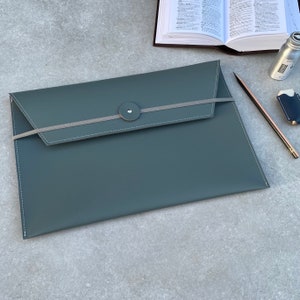 May include: A dark gray leather envelope with a gray elastic band and a silver button closure.