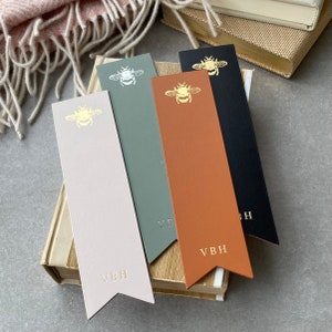 Könnte beinhalten: Vier Leder-Lesezeichen mit einem goldenen Bienen-Design und den Initialen "VBH" auf jedem. Die Lesezeichen sind in verschiedenen Farben: beige, grün, braun und schwarz.