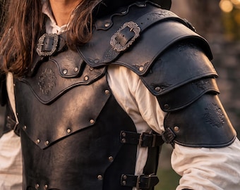Peut inclure: Une armure en cuir noir avec des boucles et des rivets décoratifs en métal. L'armure présente des épaulières superposées et une plaque de poitrine. Le design comprend des motifs floraux en relief. L'armure est portée sur une chemise blanche.