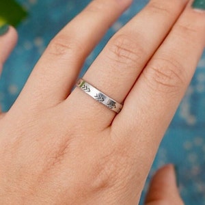 May include: A silver ring with a simple design of arrows around the band.