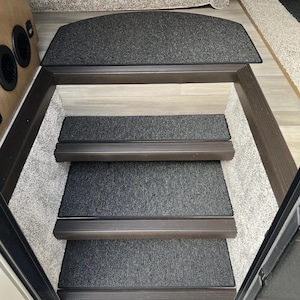 May include: A white ceramic mug with a black handle and the text "But First, Coffee" in a bold, black font. The mug is set against a blurred background, suggesting a cozy setting.