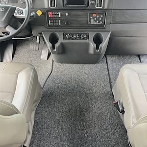 May include: A gray carpeted floor with two gray seats and a black dashboard with cup holders and controls. The dashboard has a black screen with the text "EQ" on it.
