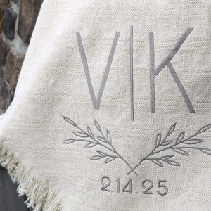 May include: A white throw blanket with a gray embroidered monogram "VK" and a date "2.14.25" below a pair of crossed branches.