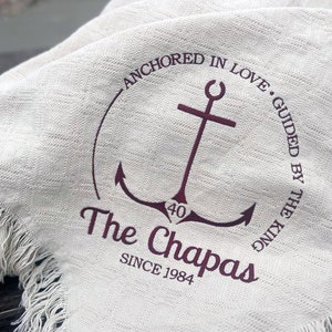 May include: A white fabric with a brown anchor design and the text "Anchored in Love. Guided by the King. The Chapas Since 1984".