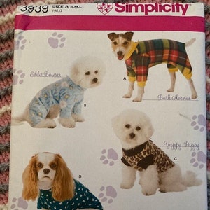 May include: A Simplicity sewing pattern for dog clothes, featuring four different dog breeds wearing various outfits. The pattern is titled "Woofy Wear by Wendy" and includes instructions for making a "Bark Avenue" plaid jumpsuit, a "Yappy Puppy" leopard print top, an "Eddie Bowser" blue and white pajama set, and a "Goochie Poochie" teal and white heart print top.