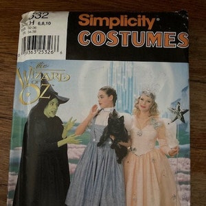 May include: A Simplicity Costumes sewing pattern envelope for The Wizard of Oz, featuring illustrations of a green-skinned witch in a black dress, a person in a blue gingham pinafore dress holding a black dog, and a person in a peach gown with a star wand.