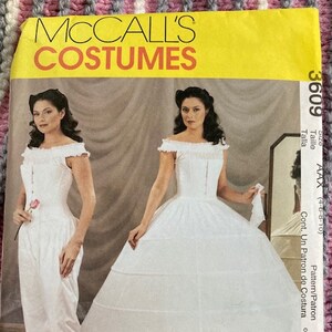 May include: A McCall's Costumes sewing pattern envelope, number 3609, featuring illustrations of two white garments: a pair of cropped trousers with lace trim and a full-length, off-the-shoulder gown with a wide, tiered skirt and lace hem.