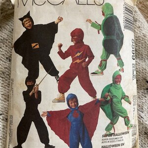 May include: A vintage McCall's sewing pattern for children's Halloween costumes. The pattern includes five different costumes: a ninja, a superhero, a turtle, a bat, and a spider. The pattern is for sizes 2 through 8. The pattern is titled "Super Halloween" and "Halloween en Grand Style".