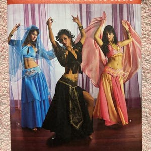 May include: Simplicity sewing pattern 2941 for The Dance Studio. The pattern features three dancers in colorful belly dance costumes. The pattern size is RR 14, 16, 18, and 20. The pattern includes the designer's name, Andrea Schewe.