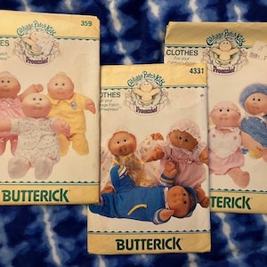 May include: Three vintage Cabbage Patch Kids sewing patterns with instructions for making clothes for the dolls. The patterns are for sizes 359, 4331, and 409. The patterns feature illustrations of the dolls wearing the clothes.