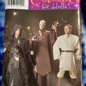 May include: A sewing pattern for adult costumes. The pattern includes three different costumes: a dark hooded robe, a long brown robe, and a white robe with a brown belt. The pattern is titled "Costumes for adults" and has the number 0579 printed on it.