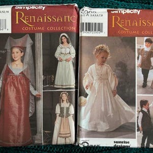May include: Two Simplicity Renaissance Costume Collection sewing pattern envelopes. The left envelope features a red gown with a headpiece and two alternative outfits. The right envelope displays a white gown and two additional costume variations.