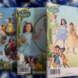 May include: Three Simplicity sewing patterns featuring Disney Fairies. The patterns showcase images of children in fairy costumes. The patterns include Tinker Bell and other fairy characters. The patterns are for home sewing.