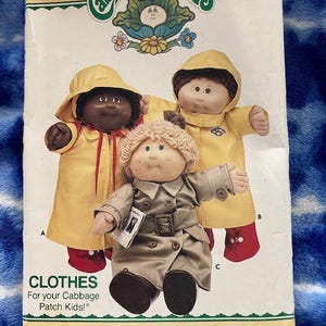 May include: A vintage Butterick pattern for Cabbage Patch Kids clothes. The pattern features illustrations of Cabbage Patch Kids dolls wearing yellow raincoats and a tan trench coat. The text reads "CLOTHES For your Cabbage Patch Kids!"