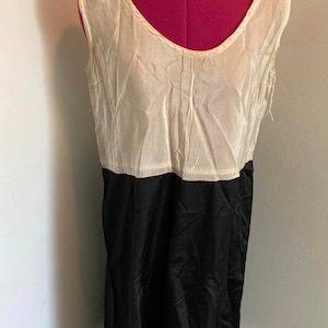 May include: A sleeveless dress with a white top and a black bottom. The dress is made of a silky material and has a simple, elegant design.