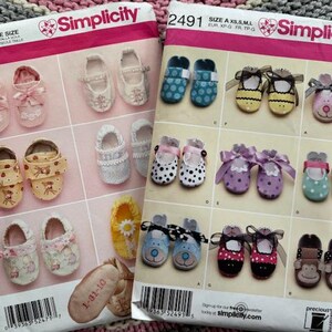 May include: Two Simplicity sewing pattern packets for baby shoes. The patterns feature various shoe designs, including those with bows, animal faces, and polka dots. The packets are labeled with the numbers 2471 and 2491.