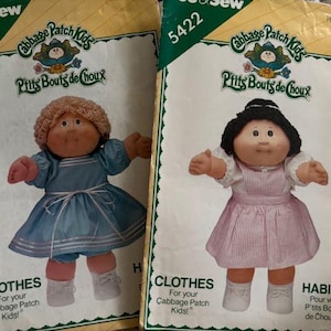 May include: Two vintage Cabbage Patch Kids pattern packets. One features a doll in a blue dress, the other in a pink dress. The packets have the text "See & Sew", "Cabbage Patch Kids", and "Clothes" printed on them.