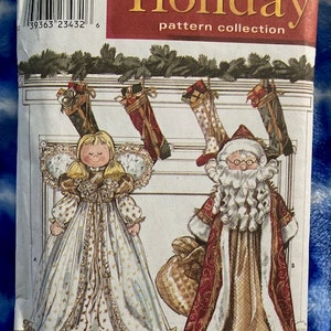 May include: Simplicity Holiday pattern collection sewing pattern for a Santa and angel doll. The pattern cover features illustrations of the dolls in front of a fireplace with stockings hanging from the mantle.