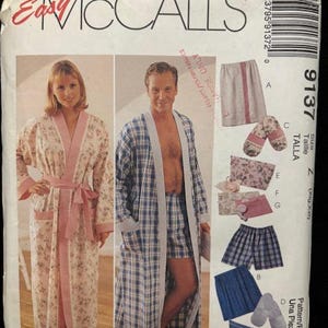 May include: McCall's sewing pattern for robes, shorts, and slippers. The pattern features a woman in a floral robe with pink trim and a man in a blue plaid robe and shorts. The pattern includes various styles and sizes.