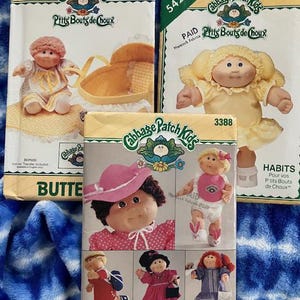 May include: Three vintage Cabbage Patch Kids sewing pattern packets. The packets feature illustrations of the dolls in various outfits. The packets are labeled with the brand name "Butterick" and "See & Sew".