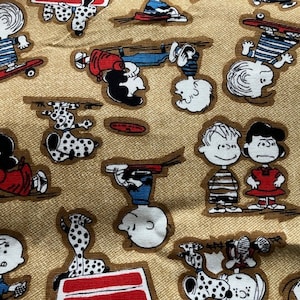 May include: A tan fabric with a repeating pattern of Peanuts characters. The characters are in various poses, including skateboarding, playing frisbee, and sitting on a bench. The fabric is a light brown color with a subtle texture.