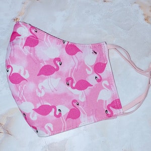 May include: Pink face mask with a flamingo print. The mask has elastic ear loops.
