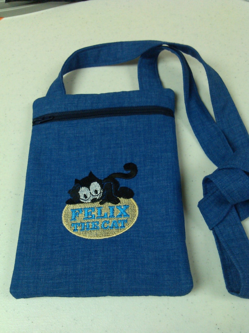May include: A blue denim crossbody bag with a zipper closure and an embroidered image of Felix the Cat. The bag has a long adjustable strap.