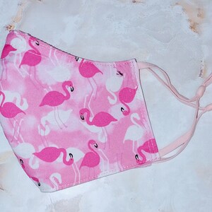 May include: Pink face mask with a flamingo print. The mask has elastic ear loops.