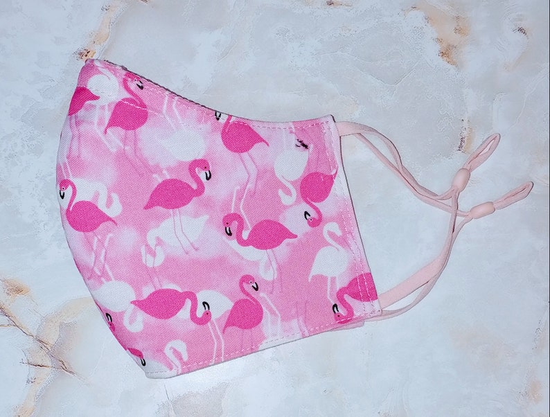 May include: Pink face mask with a flamingo print. The mask has elastic ear loops.