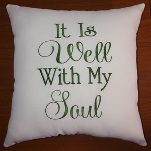 May include: White throw pillow with green embroidered text that reads "It Is Well With My Soul".