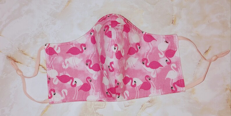 May include: Pink face mask with a flamingo print. The mask has elastic ear loops.