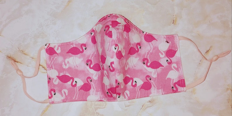 May include: Pink face mask with a flamingo print. The mask has elastic ear loops.